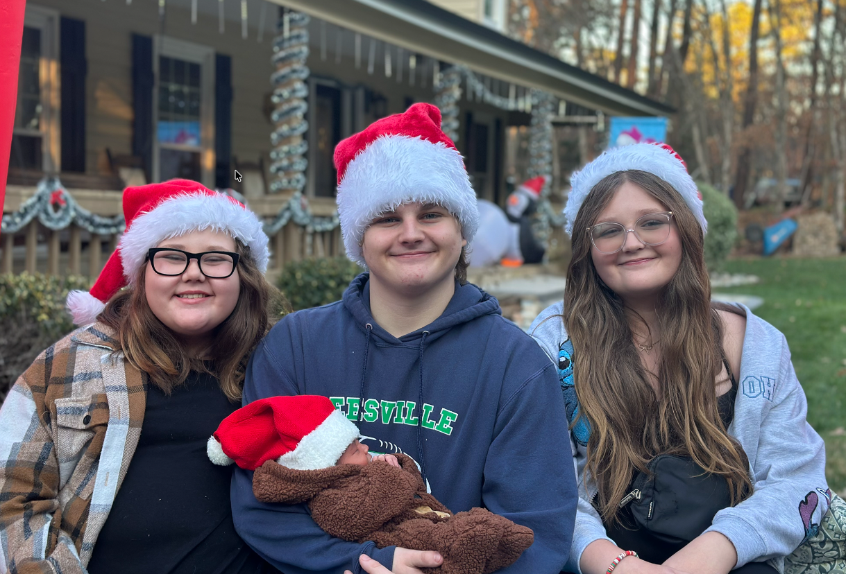 Trey with family at Christmas, holding a newborn, wearing Santa hats.